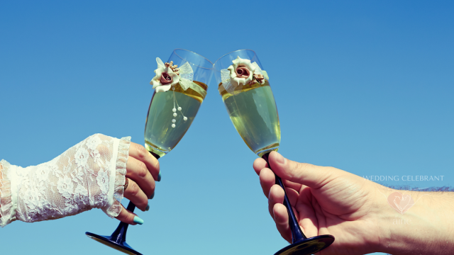 Bride and groom toasting with decorated champagne glasses against a blue sky